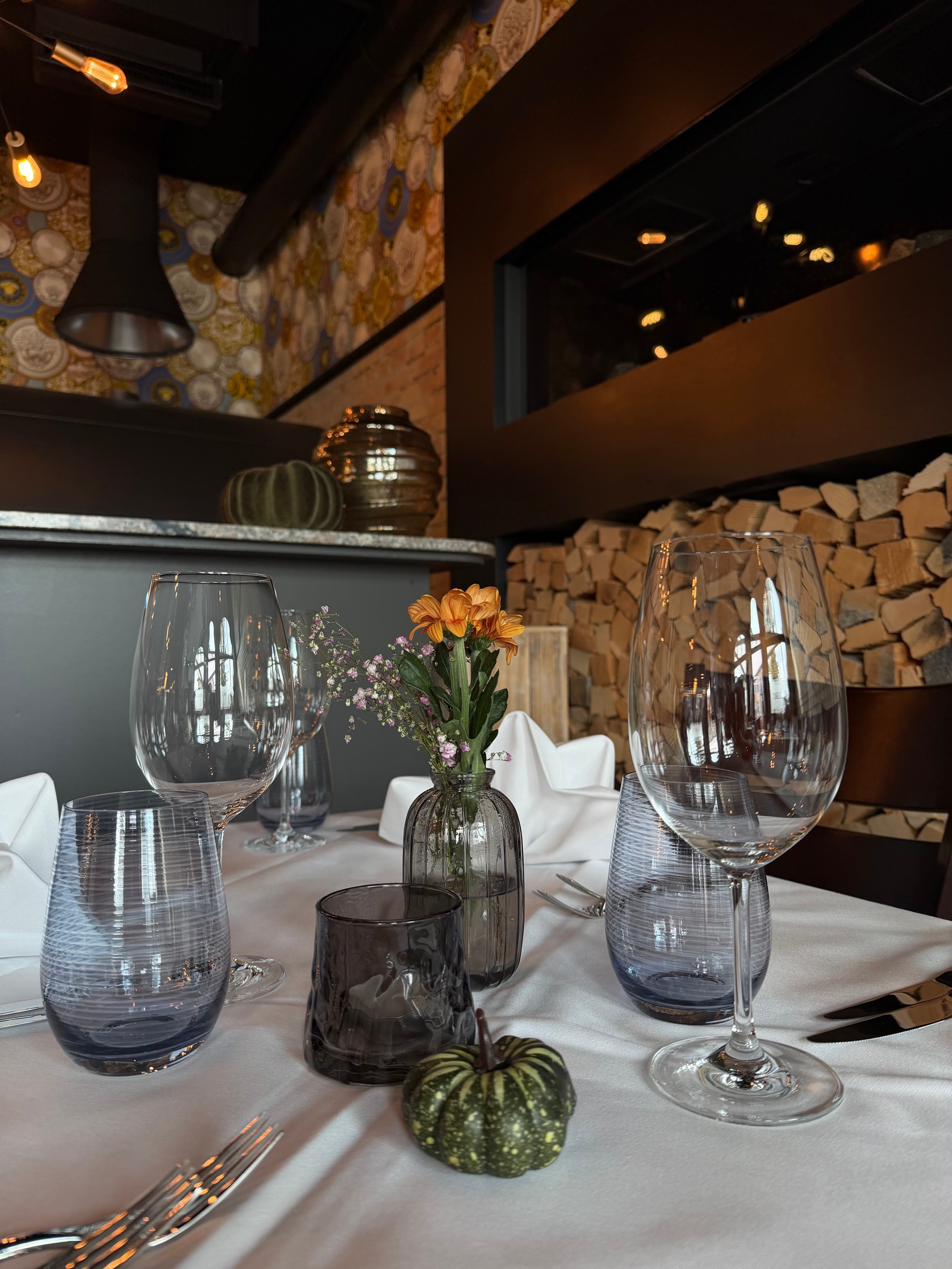Glasses on a laid table, the stacked firewood behind them