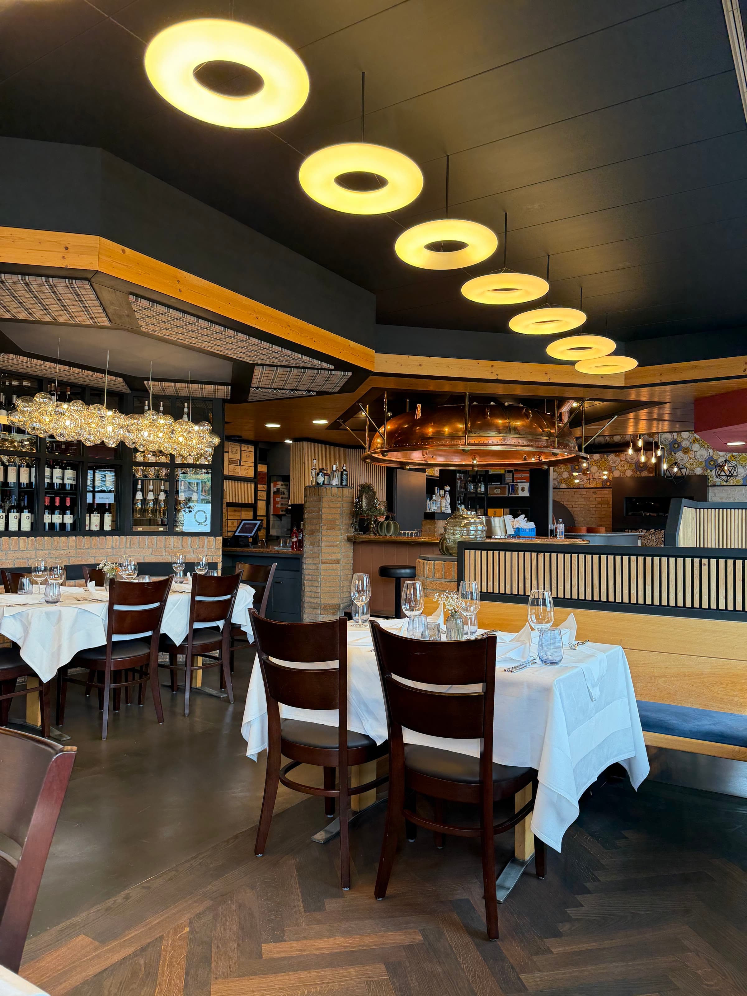 The dining room under its lamps, the tables running to the bar