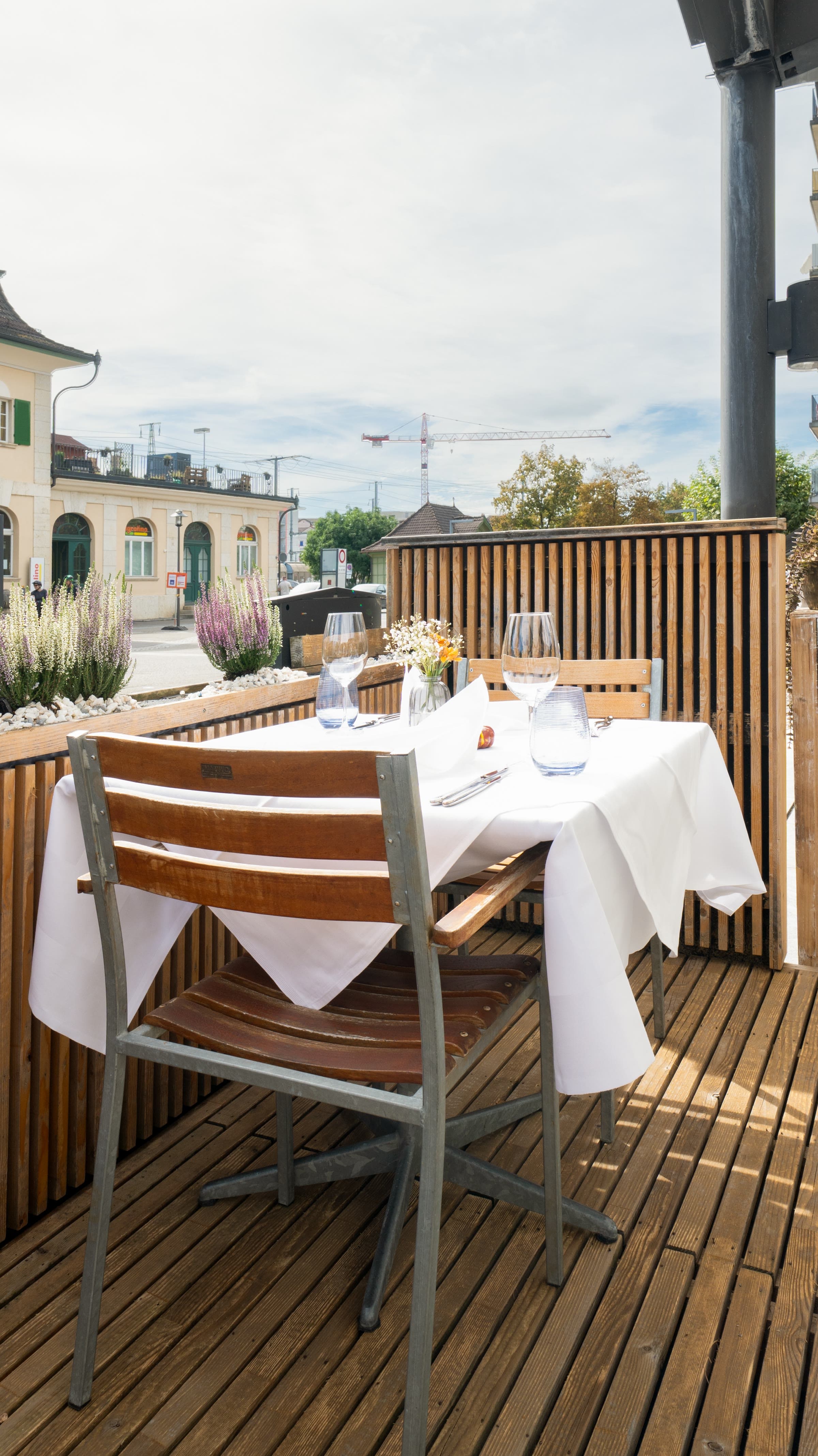 A laid table on the terrace, decking and flowers behind it